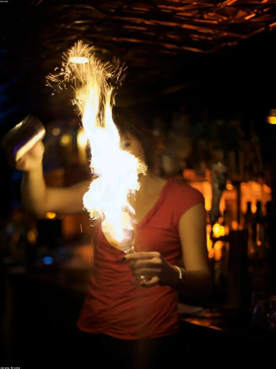 A bartender pouring a flaming flair stream behind a dark bar